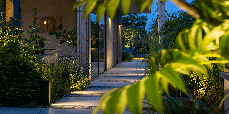 Gartenbeleuchtung in Form von Stehleuchten und Wandlampen beleuchtet den Weg neben einem Haus.