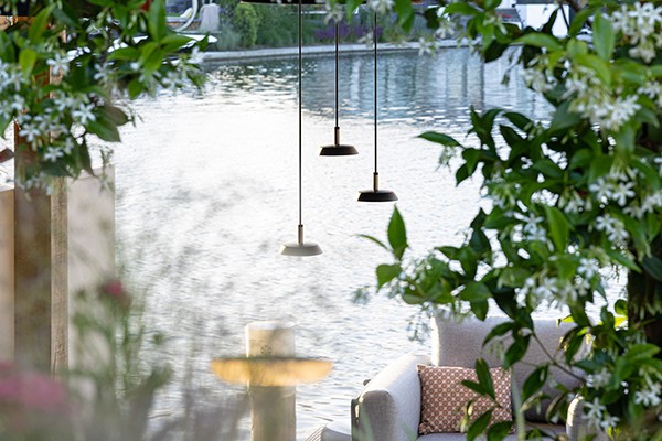 Dekorative Pendelleuchten, die au&szlig;en als Beleuchtung unter einer Pergola angebracht wurden. Im Hintergrund sieht man Pflanzen und einen See.