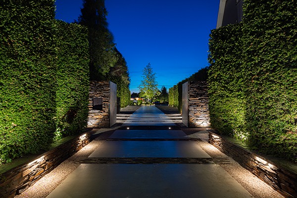Eine von Hecken und Mauern gesäumte Einfahrt mit stimmungsvoller Beleuchtung bei Nacht.
